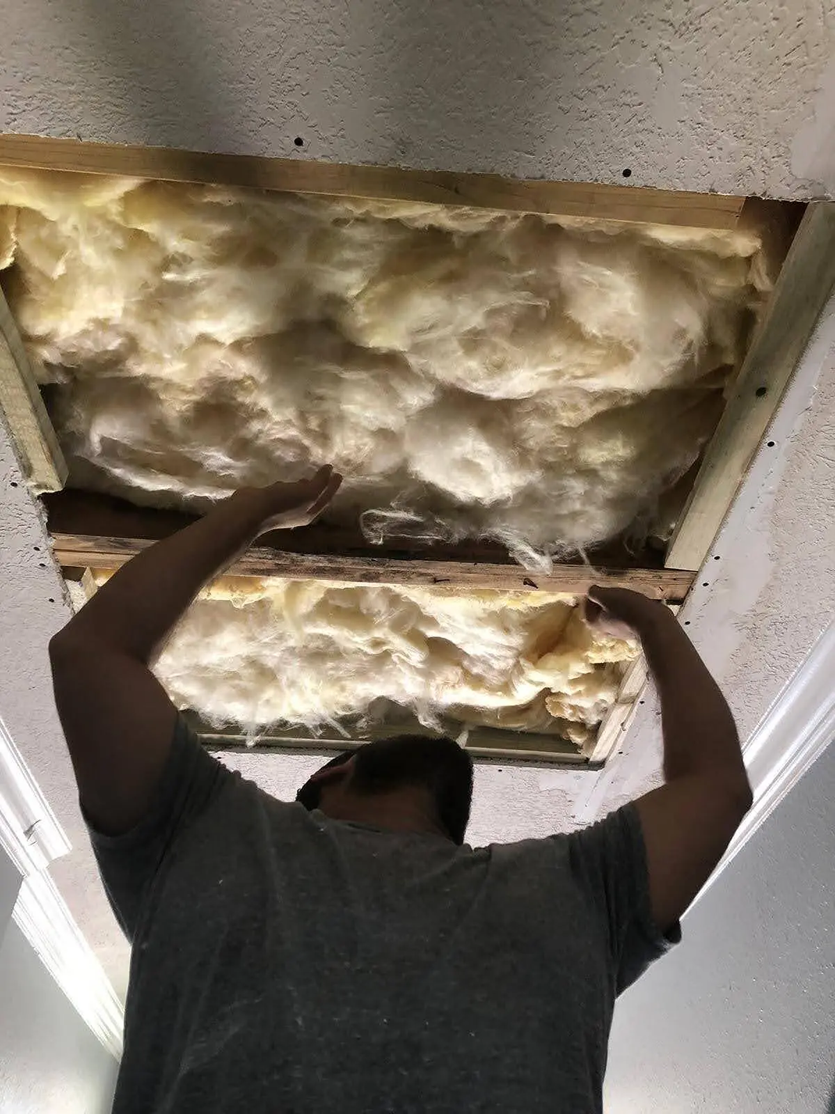 Houston tradesman packing fiberglass insulation into an exposed ceiling cavity mid-job